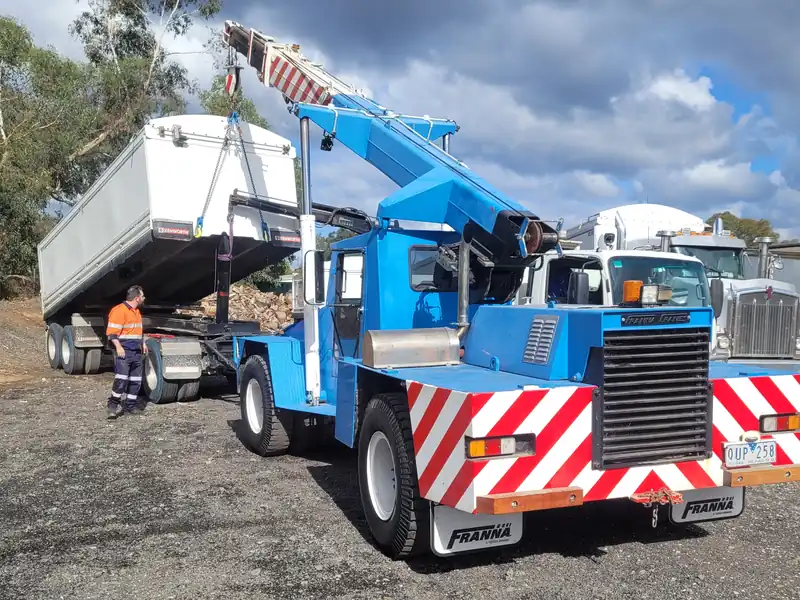 Blue Franna crane lifting a load off a truck while a worker in hi-vis watches