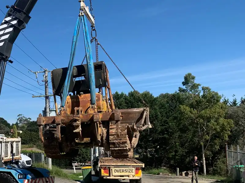 Crane lifting a large bulldozer onto the back of an oversize truck